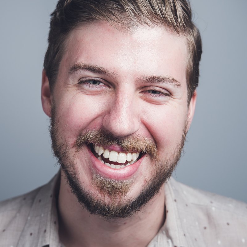 Adam Jacob Johnson, laughing, in a dotted shirt against a grey backdrop